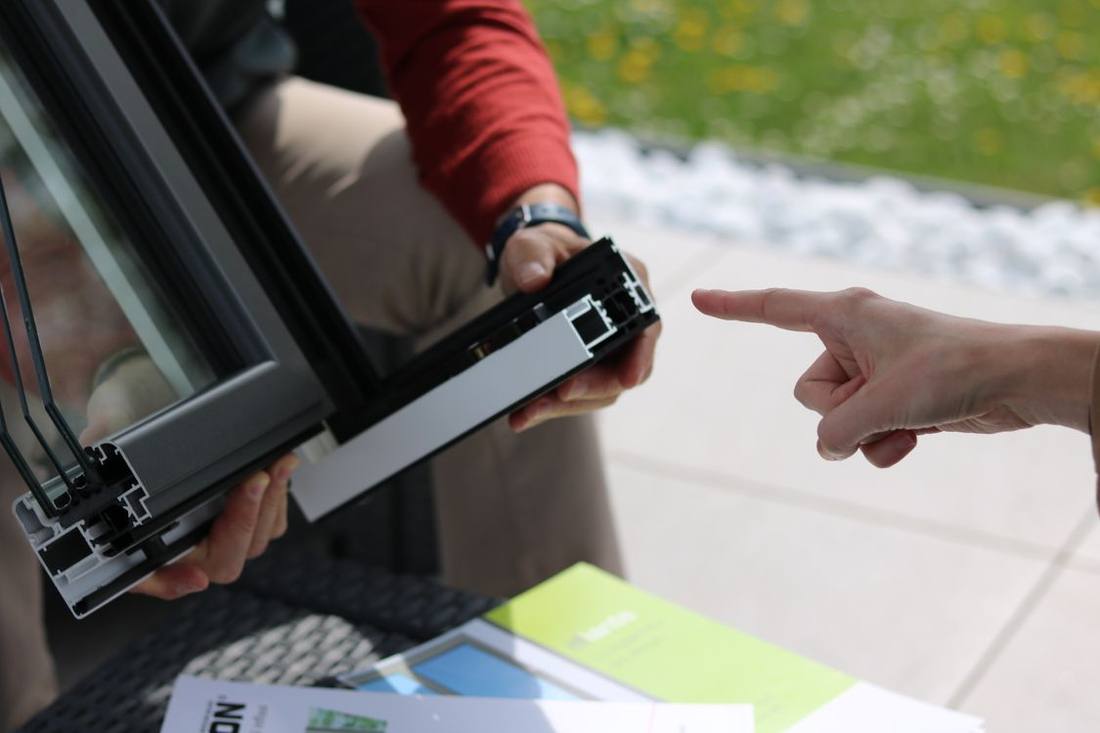 People examining a cut sample of an aluminium window frame