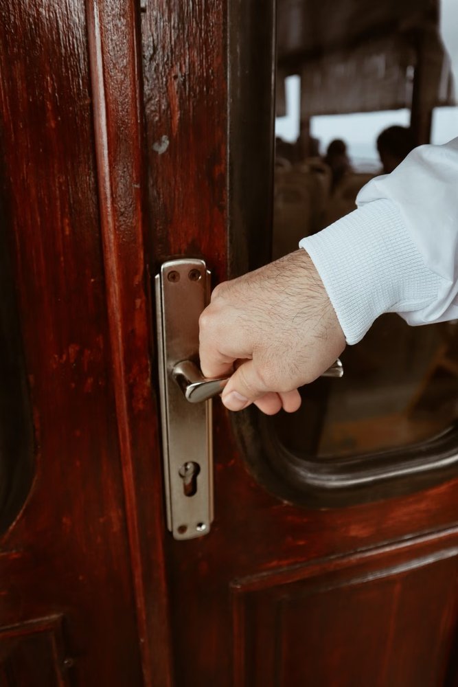 Hand operating a brass handle on a wooden door