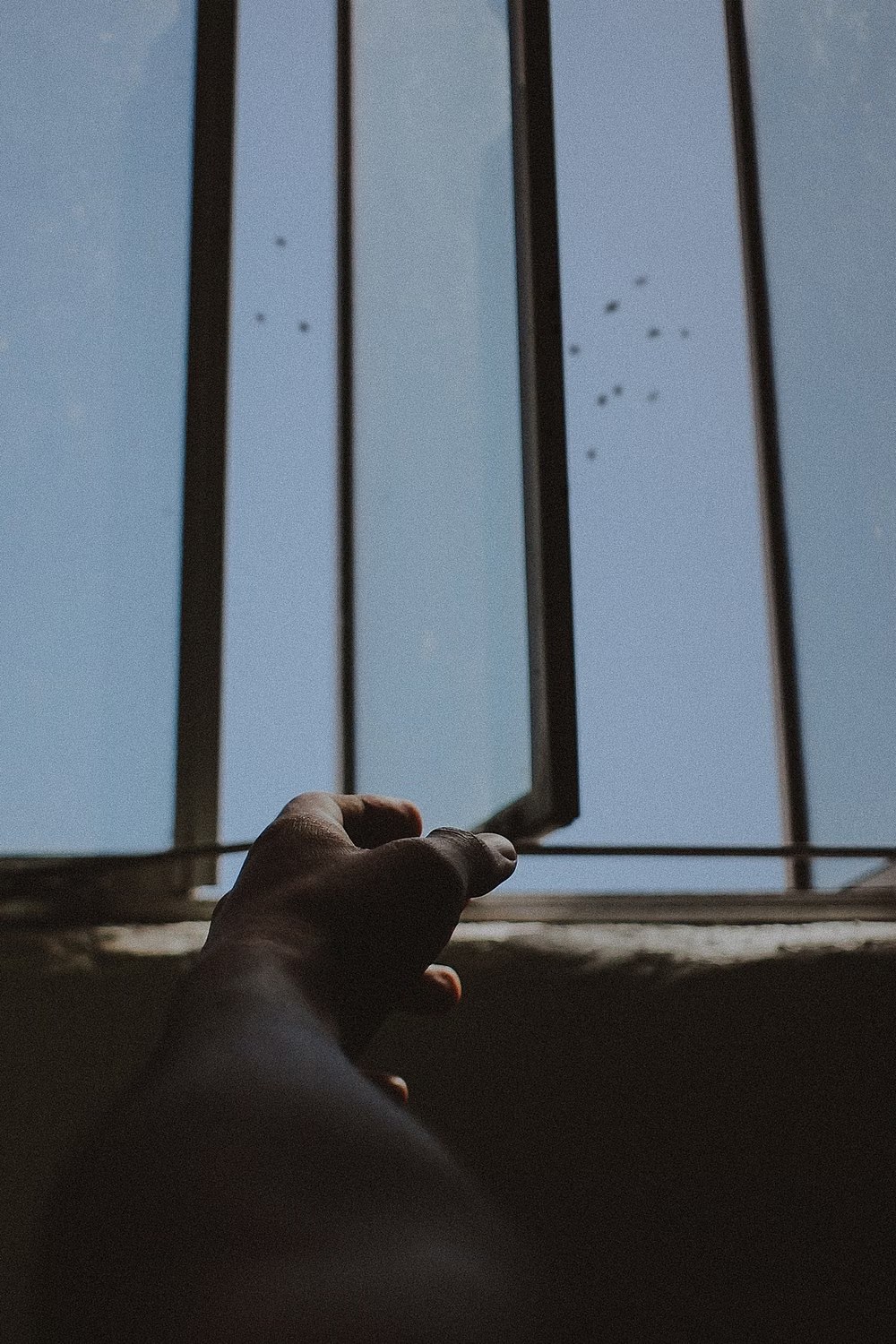Hand opening a window with birds flying in a blue sky