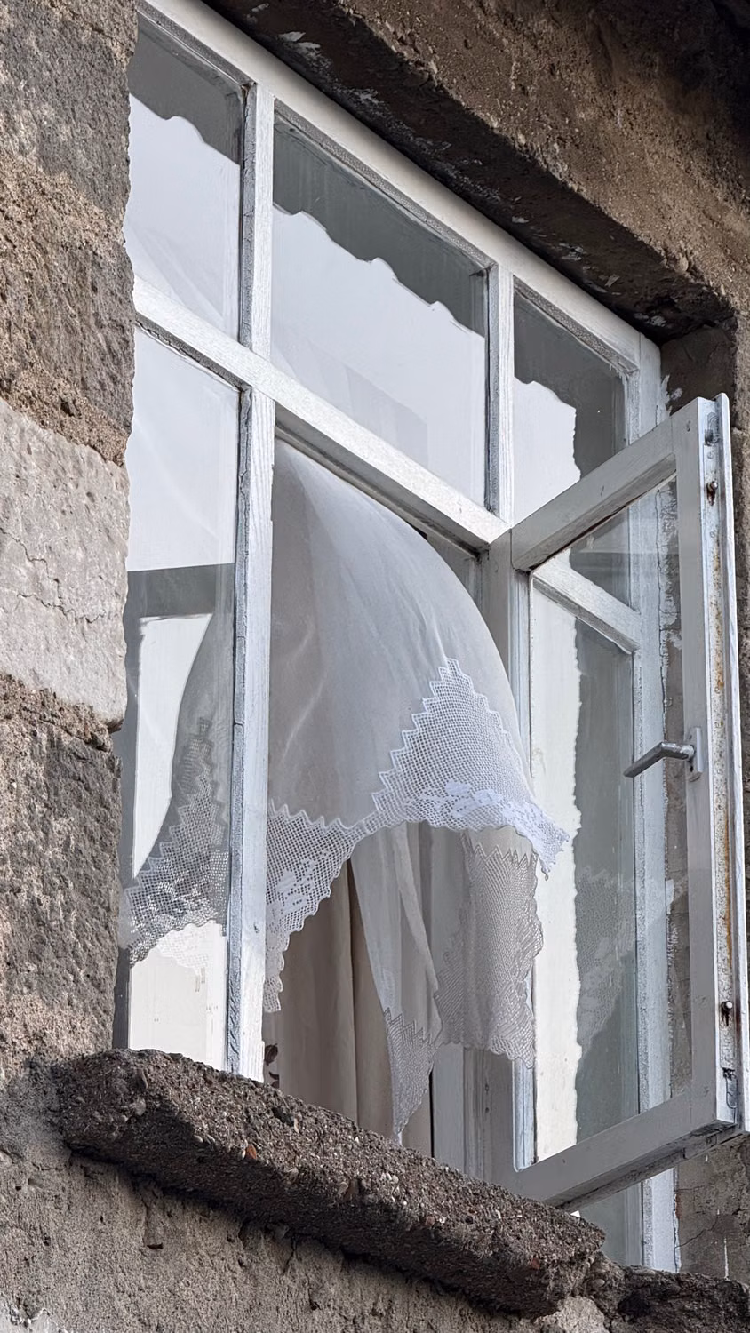 Open window with a white curtain moving in the breeze